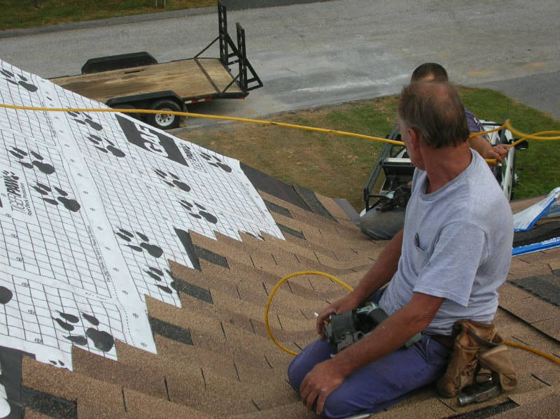 Two people working on roofing installation for a house.