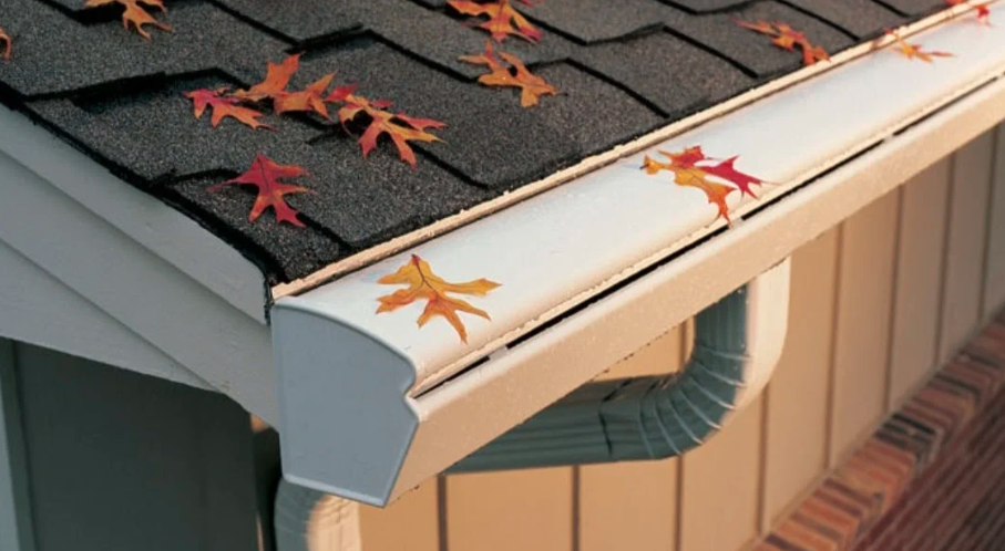 A photo of a house gutter with metal gutter guards installed. Leaves are visible on top of the gutter guards.
