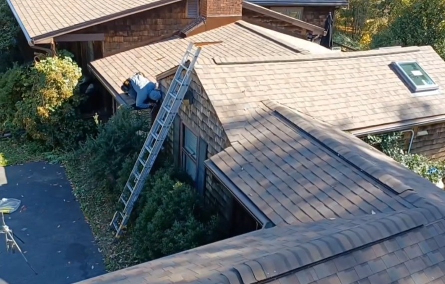 Aerial view of a roof being repaired. Sunrise Cedar shingle roof with a worker and a ladder reaching up from the ground.